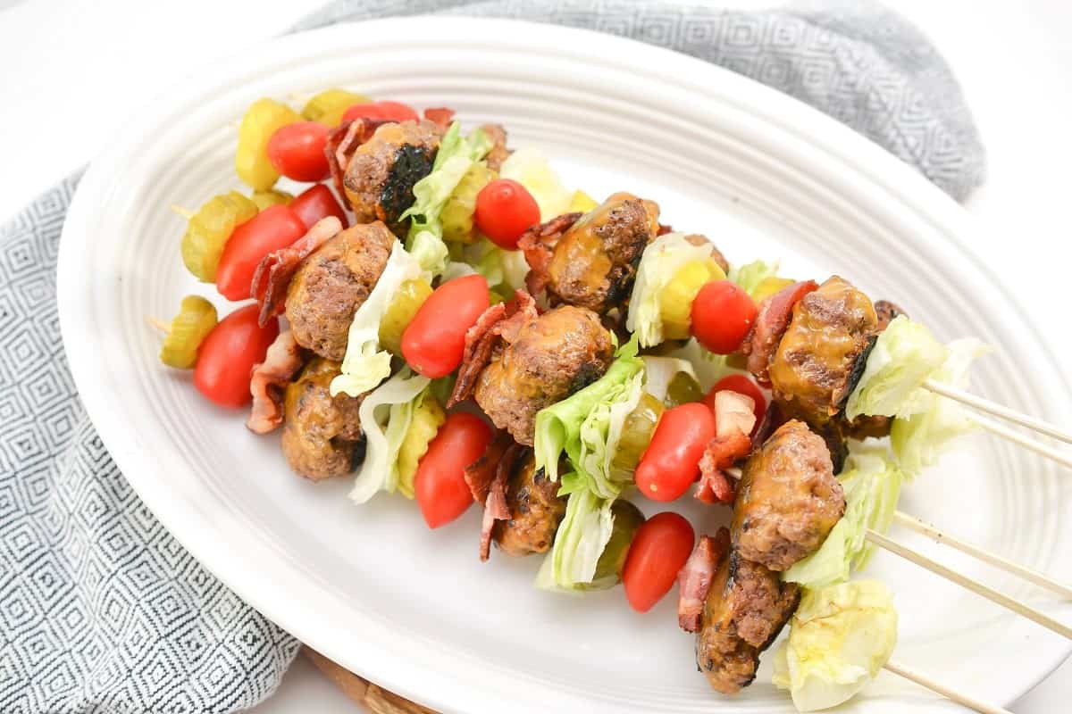 Meatball skewers on a plate with lettuce and tomatoes.