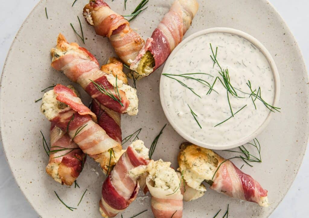 Bacon wrapped pickles with dill dip on a plate.