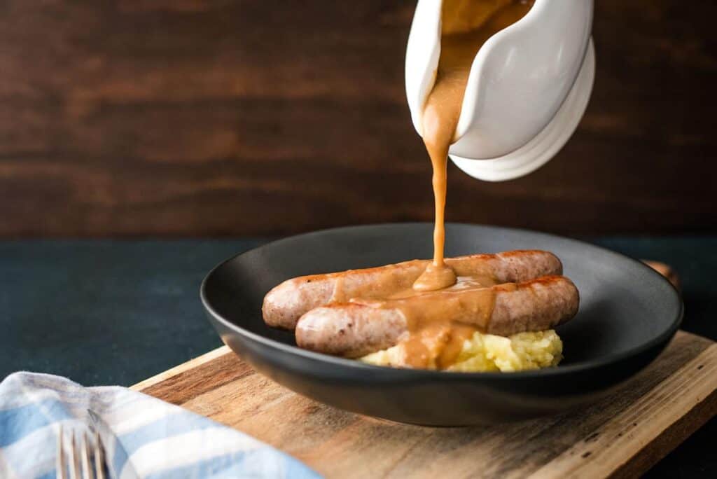 Gravy being poured over sausages and mashed potatoes.