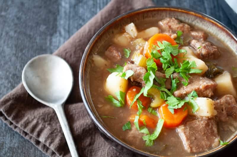 A bowl of beef stew with carrots and parsley.