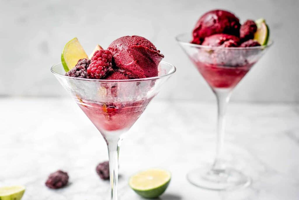 Two martini glasses filled with berries and limes.