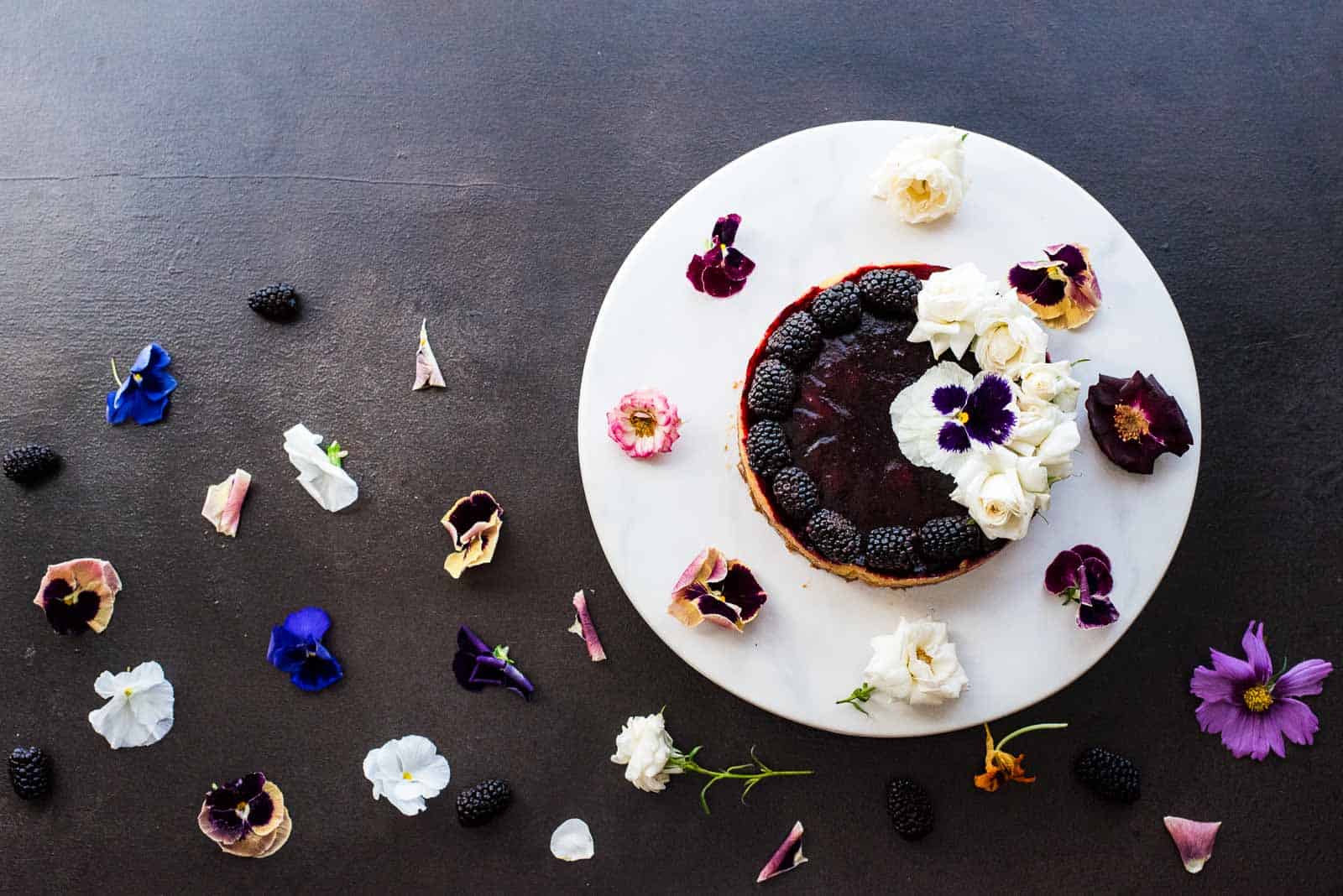 Overhead shot of a blackberry lime tart on a white plate surrounded by edible flowers.