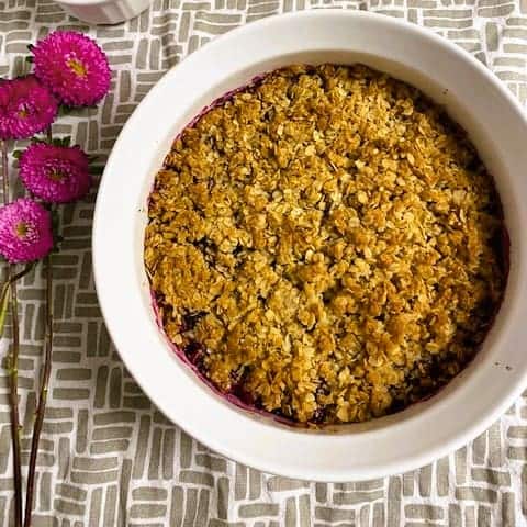 A bowl of berry crumble sitting next to flowers.