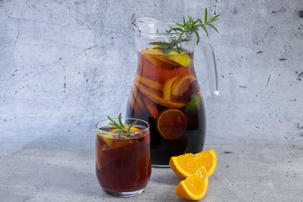 A pitcher of sangria with orange slices and sprigs of rosemary.