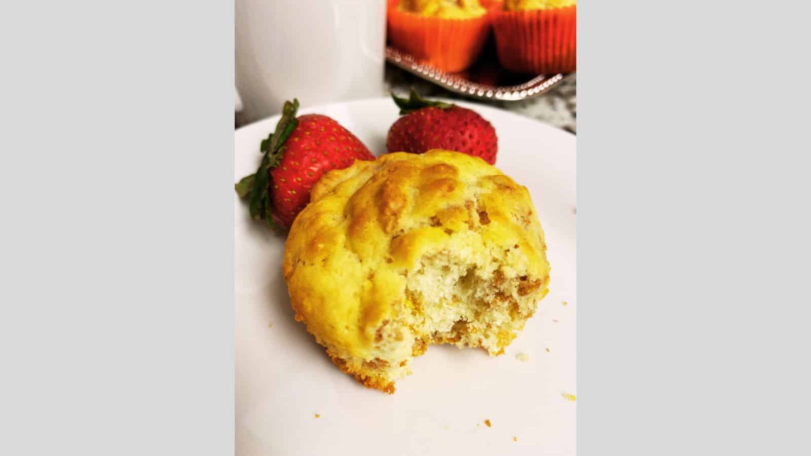 Bran muffin with a bite taken out of it on white plate with strawberries.