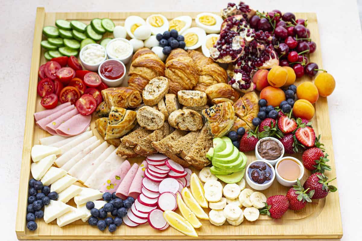 A wooden board with a variety of fruits, vegetables, and other fruits and baked goods on it.