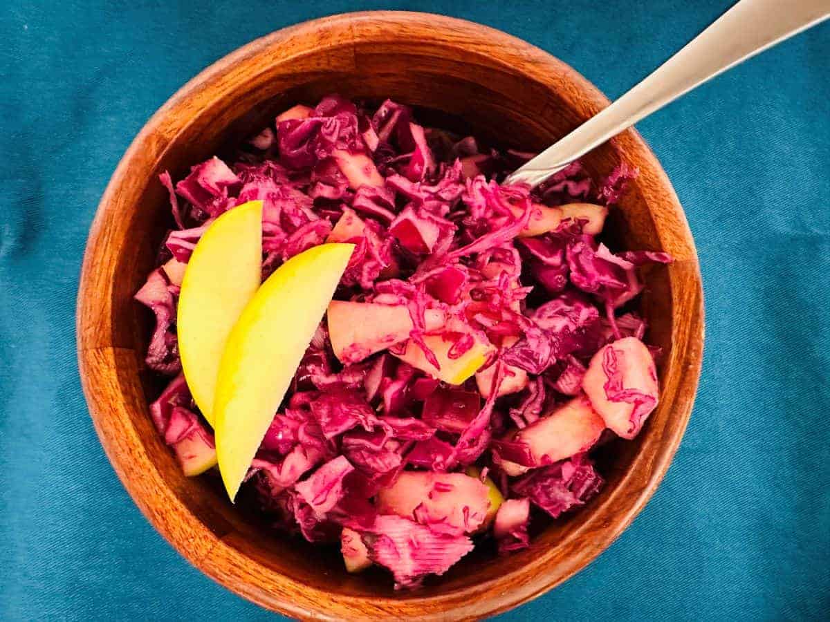 Red cabbage slaw in a wooden bowl with a spoon.