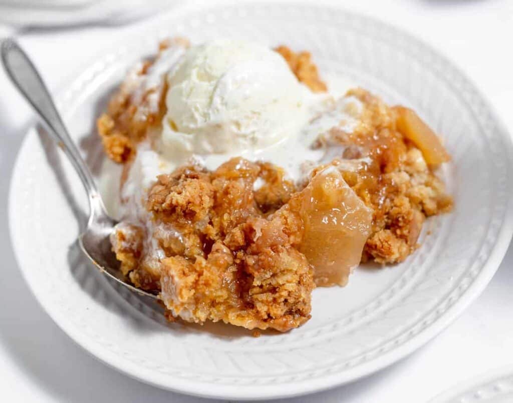 Apple crisp on a white plate with ice cream.