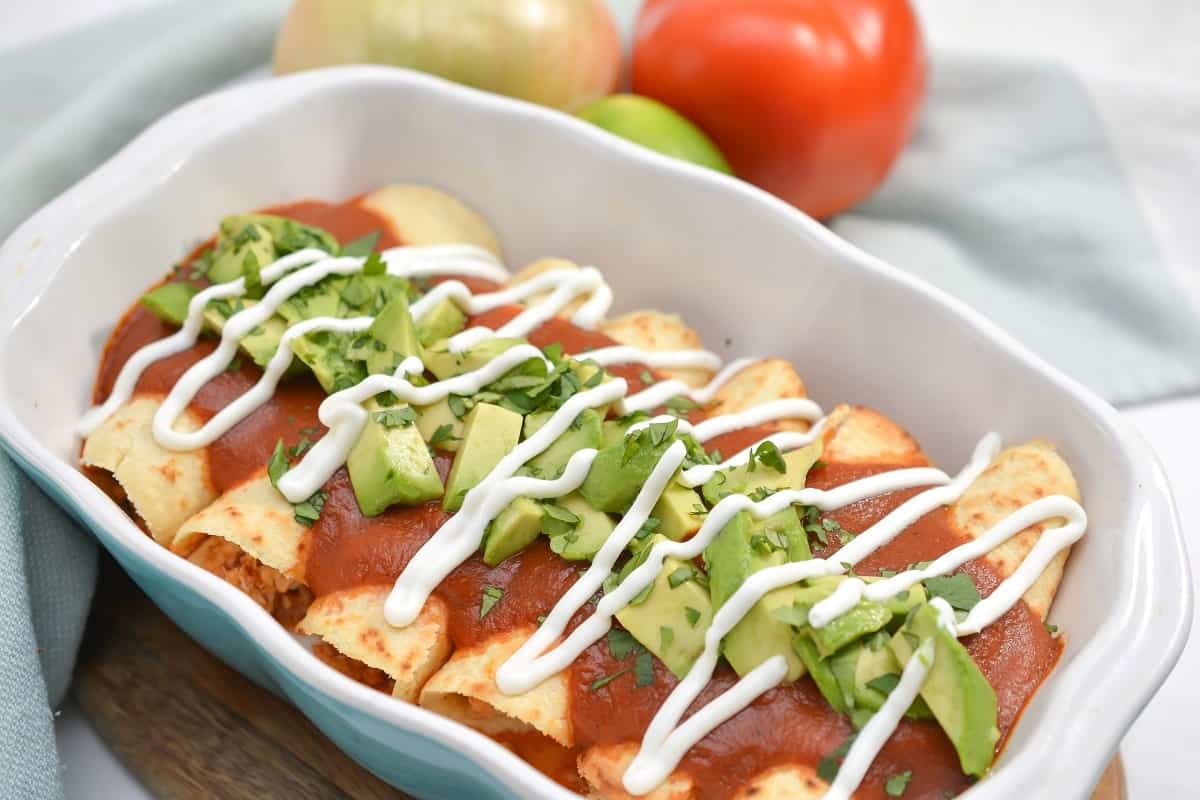 Enchiladas with avocado and tomatoes in a white dish.