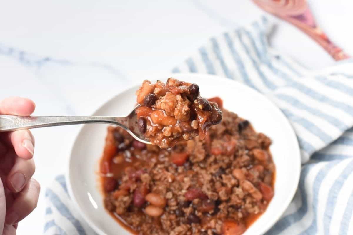 A person holding a spoonful of chili in a bowl.