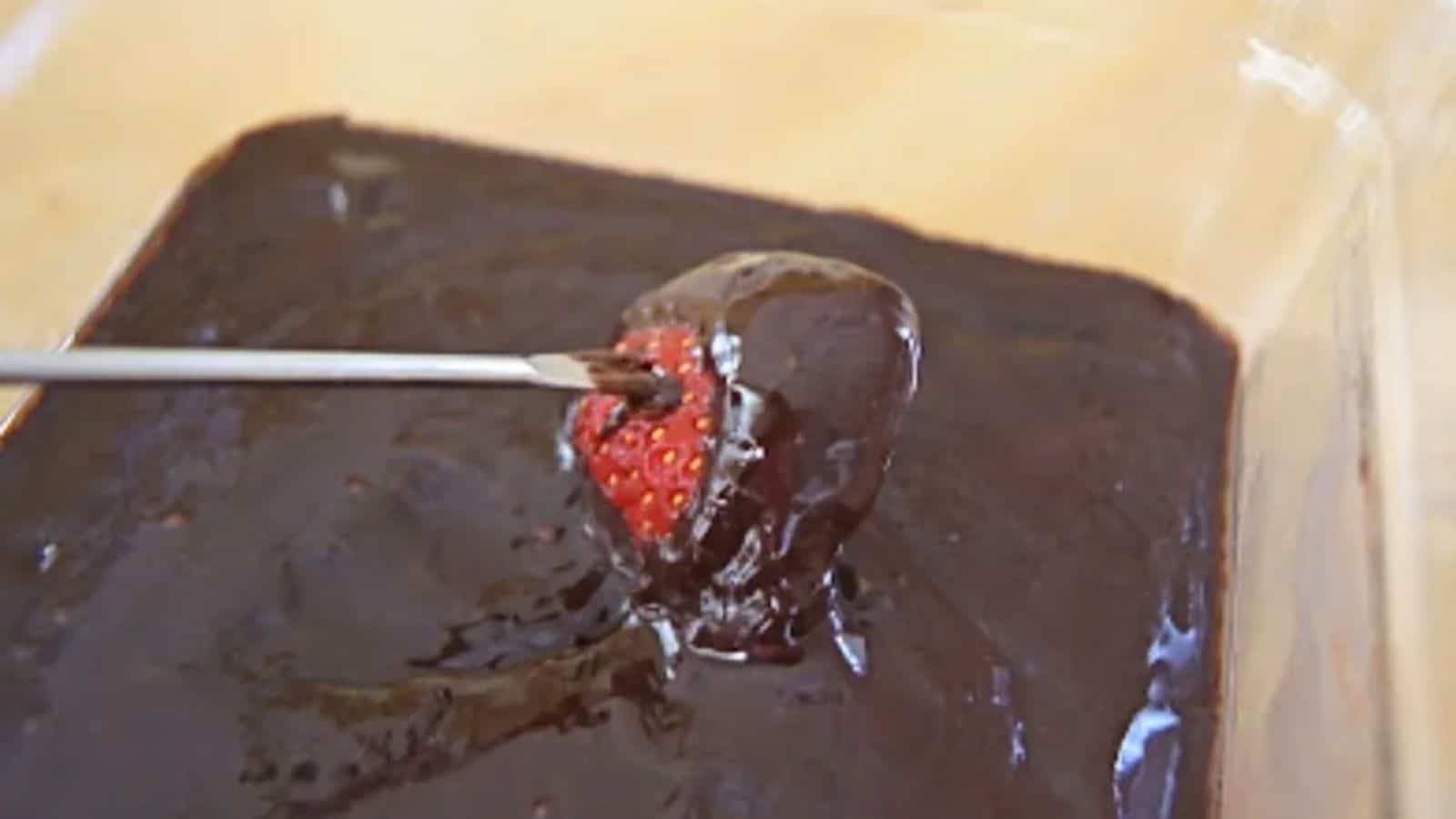 Image shows a fondue fork dipping a strawberry into chocolate fondue.