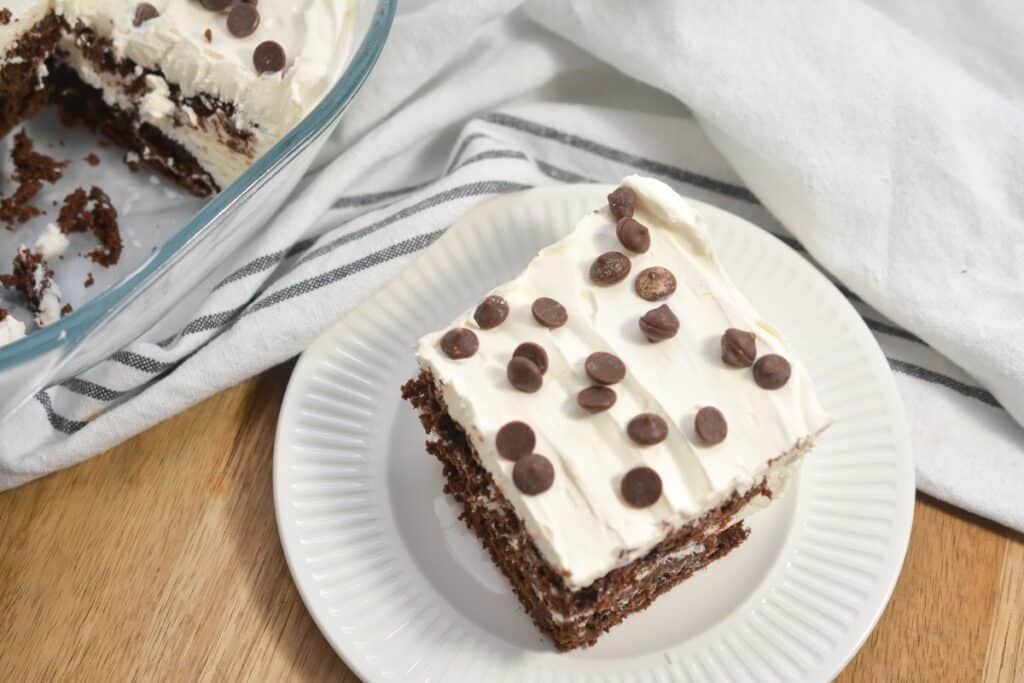 A piece of cake with frosting and chocolate chips on a plate.