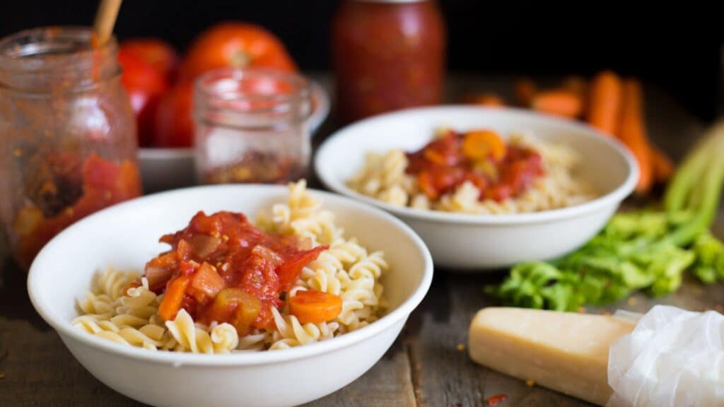 Two bowls of pasta with tomato sauce on a wooden table.