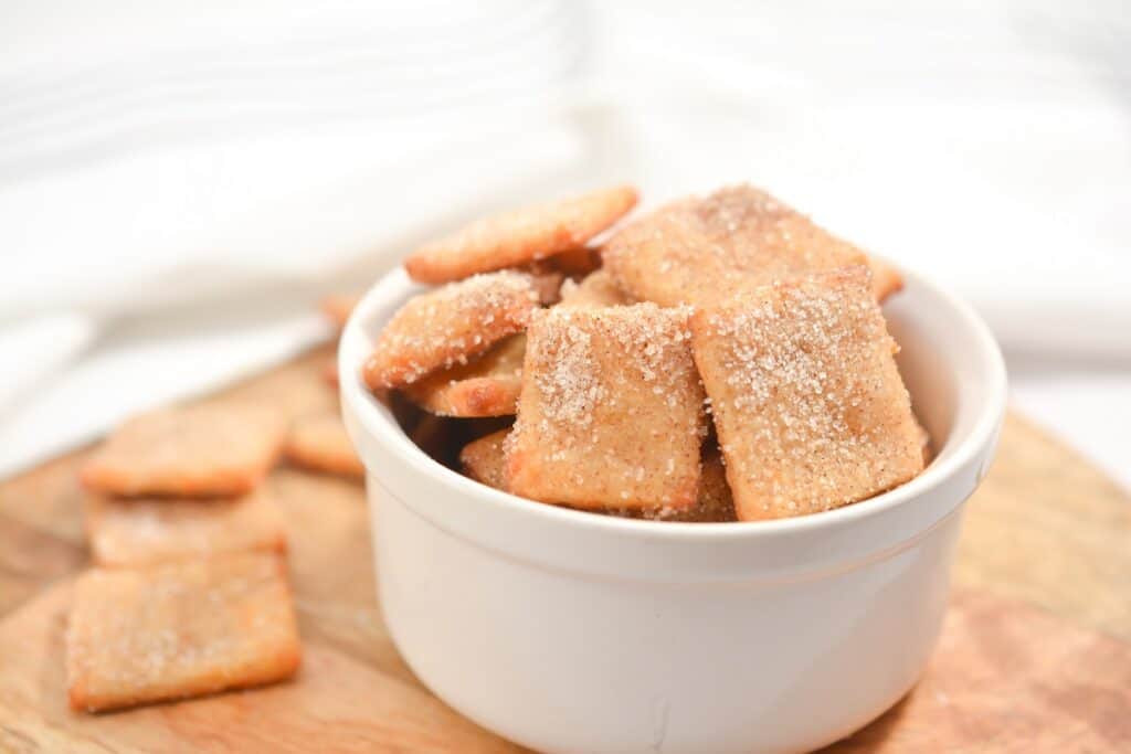 A bowl full of sugared crackers on a wooden cutting board.