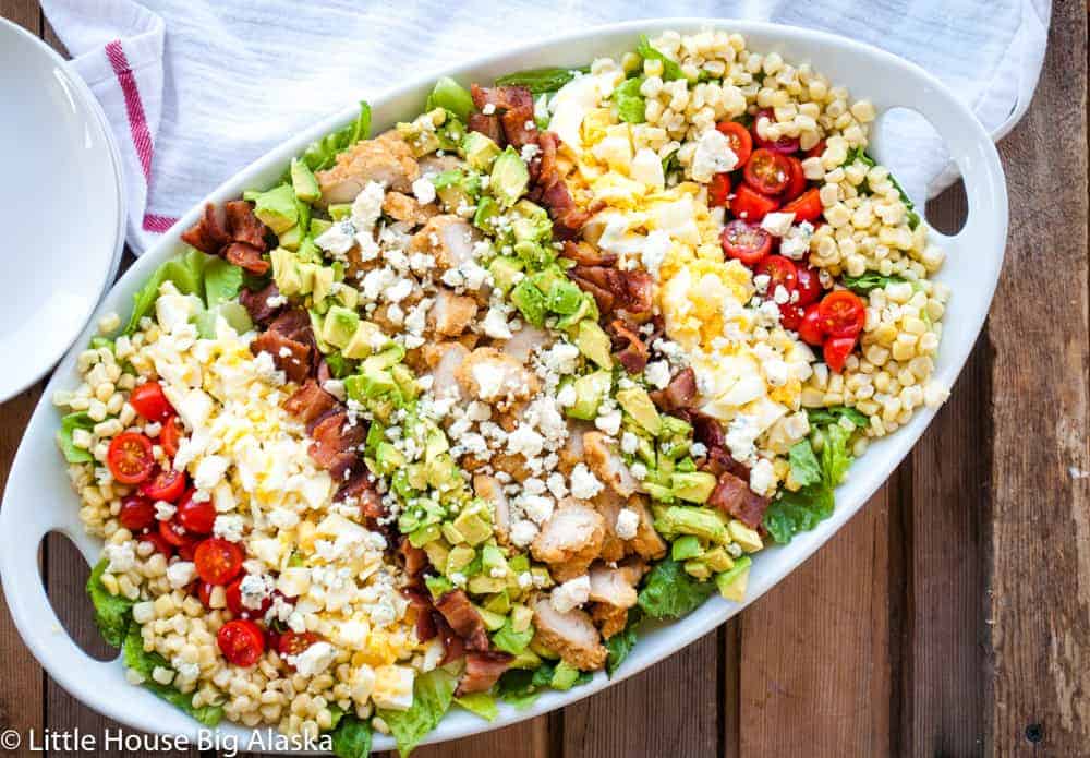 A salad with chicken, corn, tomatoes and avocado on a white plate.