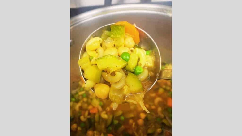 A spoon full of minestrone soup with vegetables in it.