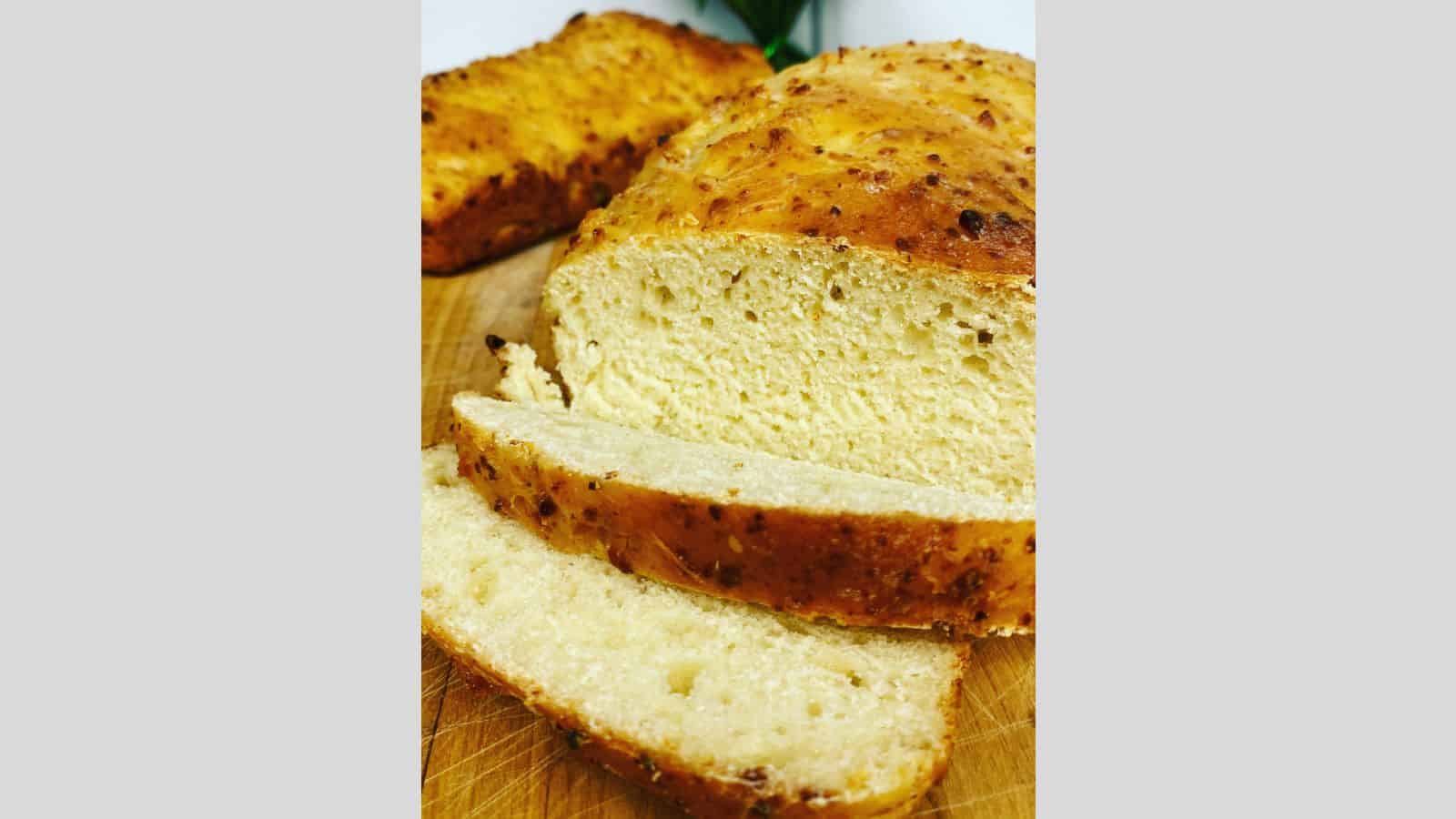 Loaf of cottage cheese bread with two slices resting on wooden board.