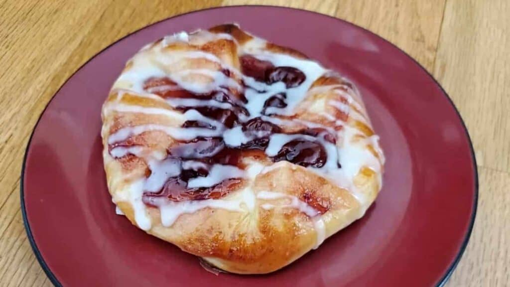 A pastry with cherries and icing on a plate.