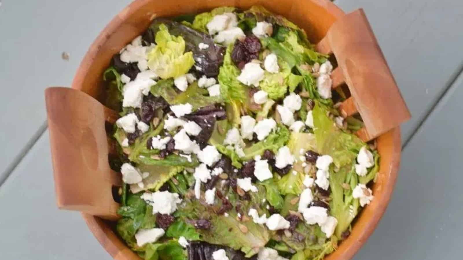 Image shows an overhead shot of a goat cheese and dried cherry salad in a wooden bowl.