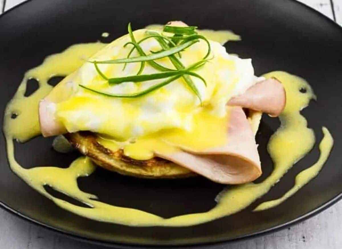 Ham and egg benedict on a black plate.