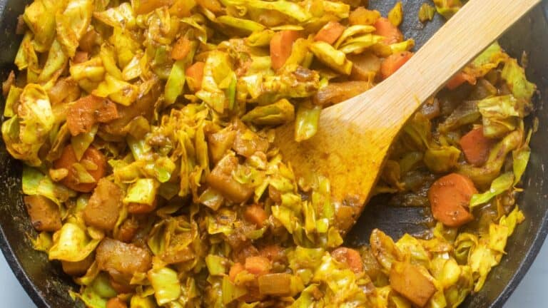 Cabbage and carrots in a skillet with a wooden spoon.