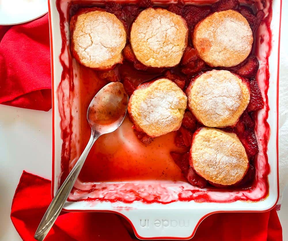 Strawberry cobbler in a baking dish with a spoon.