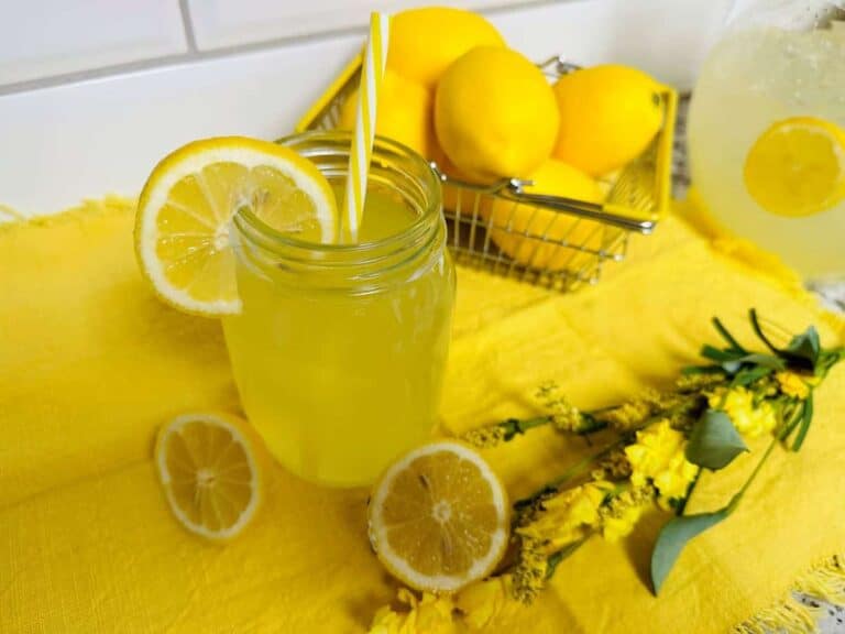 Lemonade in a mason jar with lemons and flowers.