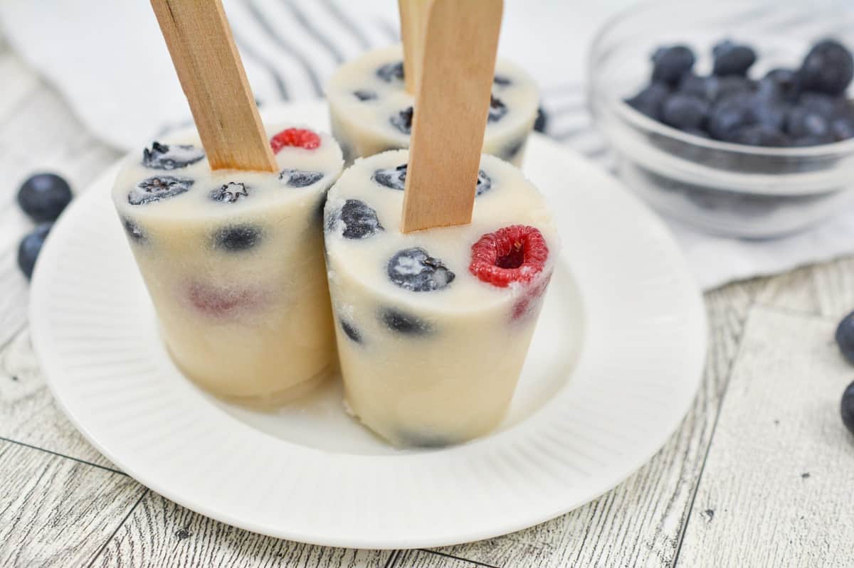 Three popsicles with blueberries and raspberries on a plate.