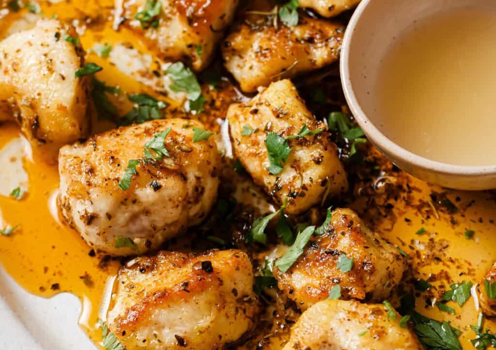 Chicken bites with garlic butter sauce and herbs on a plate.