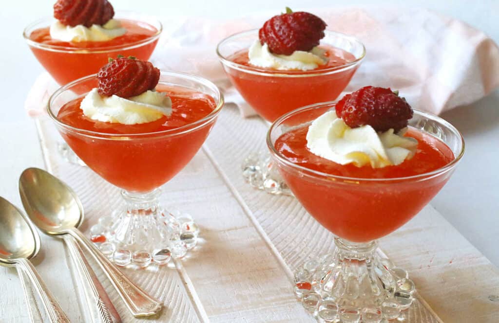 Four small glasses with whipped cream and strawberries.