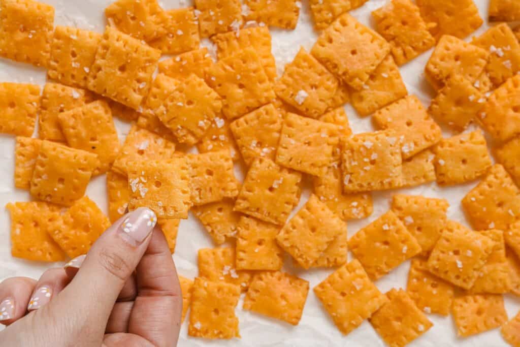 A person holding a cheesy cracker.