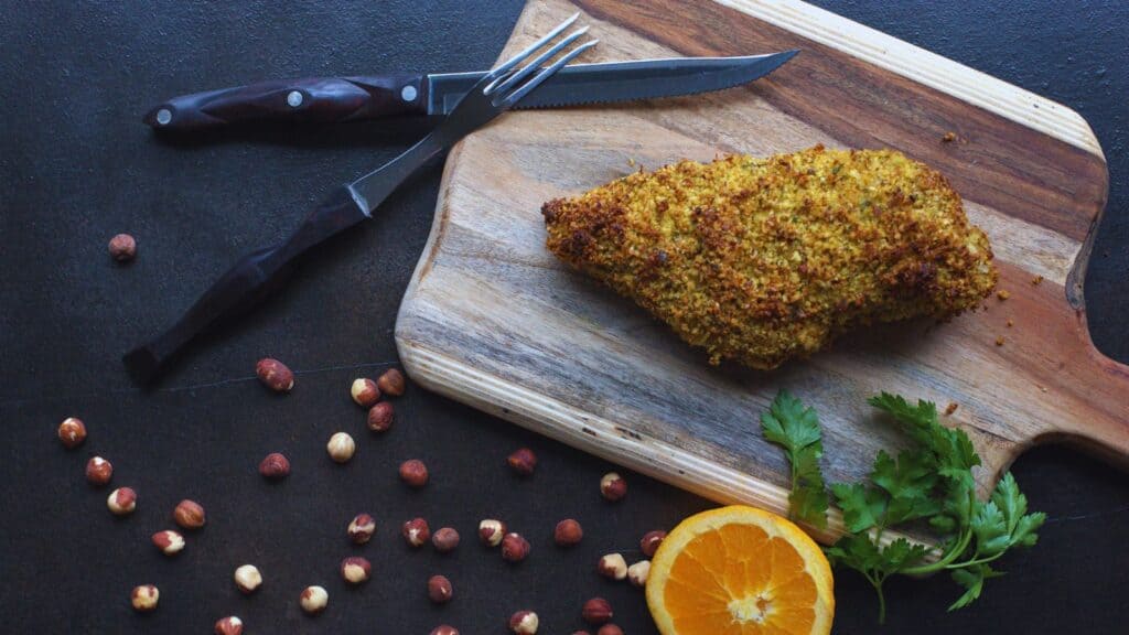 A wooden cutting board with a piece of herb crusted turkey breast and a knife.