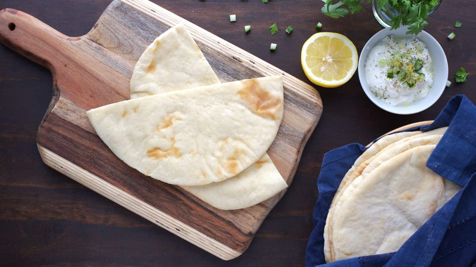 A wooden cutting board with pita bread and lemon wedges.