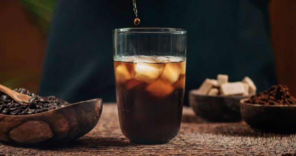 An iced coffee is being poured into a glass.