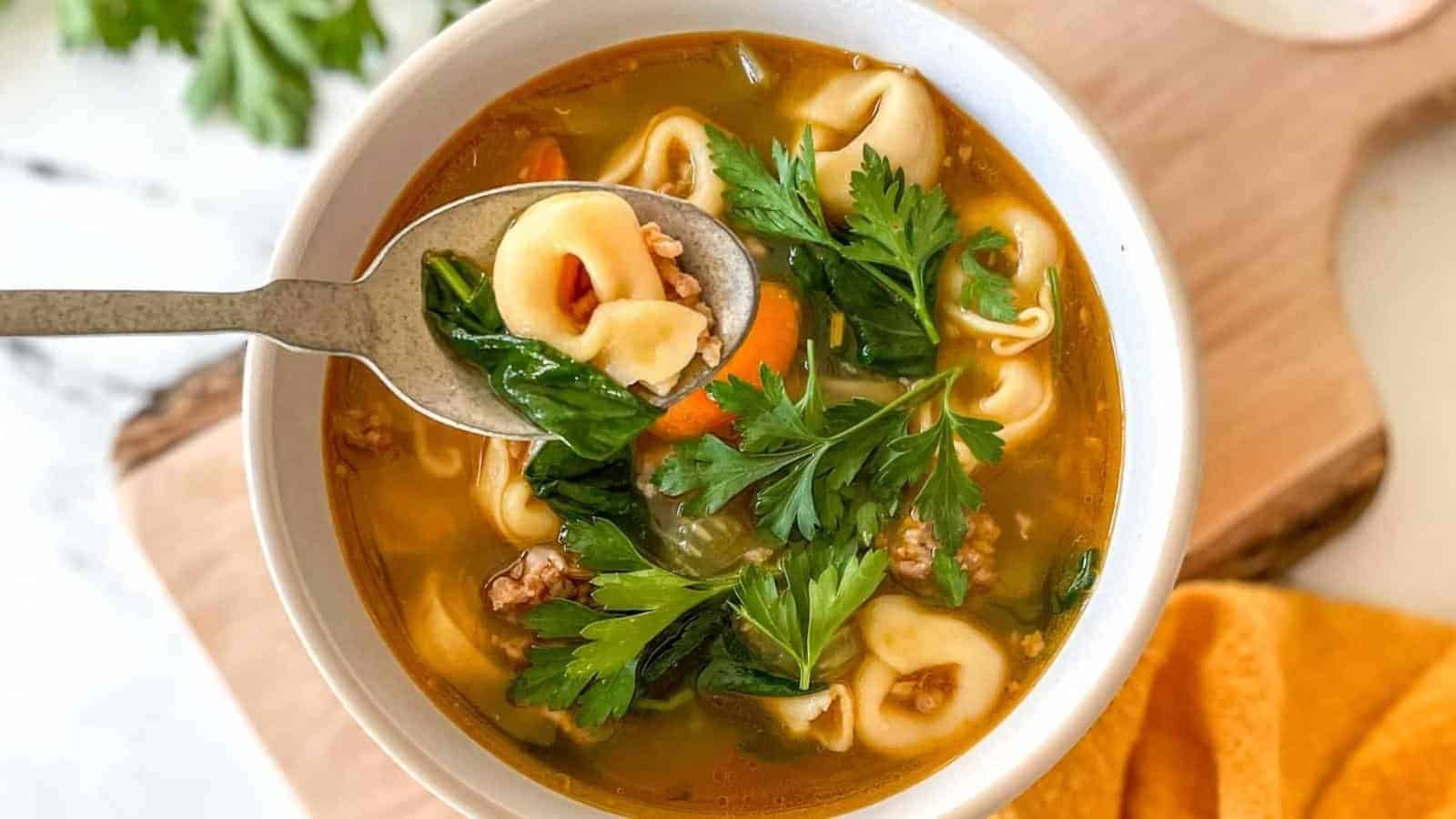 A bowl of tortellini soup sits on a rustic wooden cutting board with a yellow linen and a bunch of parsley.