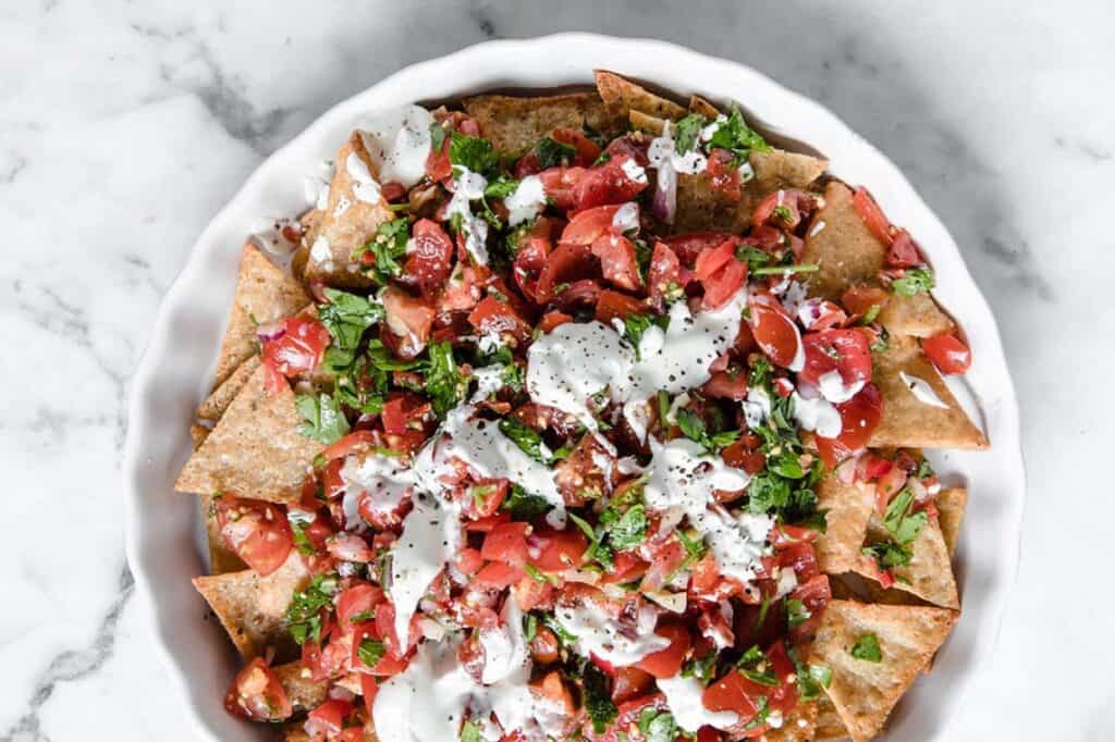 Nachos in a white bowl with tomatoes and sour cream.