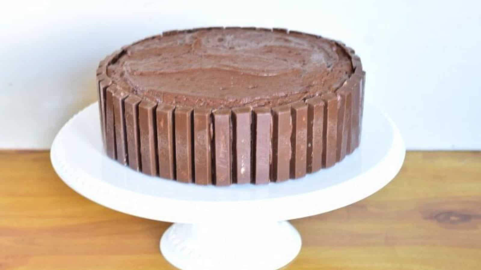 Image shows A chocolate Kit Kat cake on top of a white cake stand.