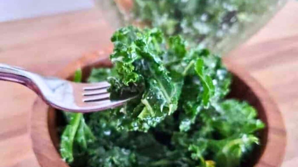 Image shows a fork holding a bite of lemon kale salad with the full bowl behind it.