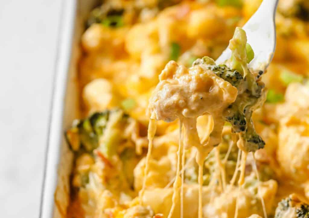 A fork is being lifted out of a casserole dish with broccoli and cheese.