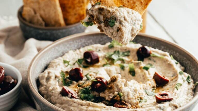 A bowl of hummus with pita chips and olives.