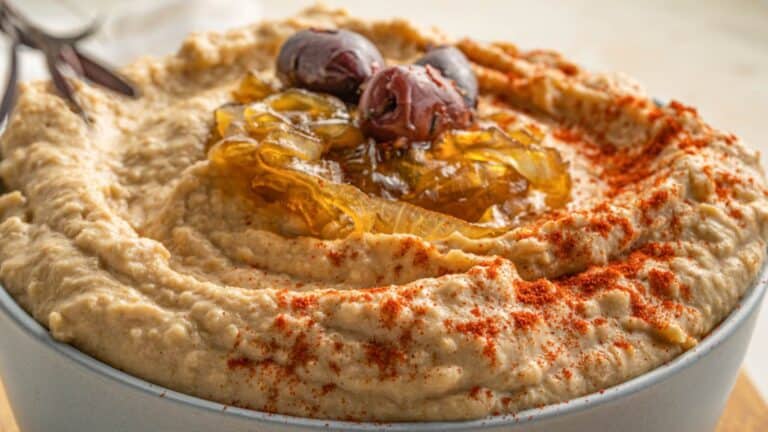 A bowl of hummus with olives and spices.