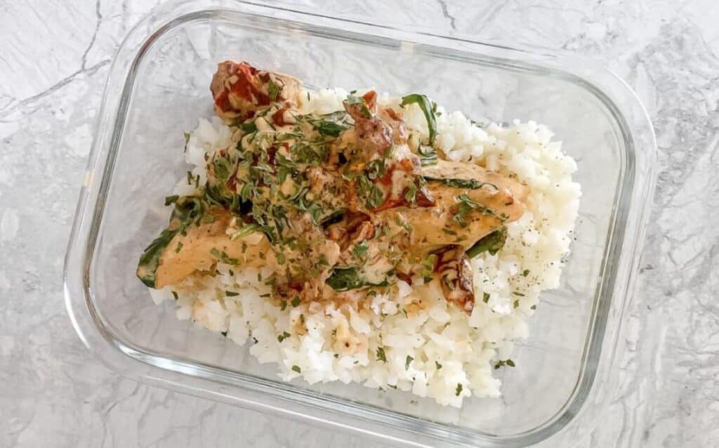 Tuscan chicken and rice in a glass container.