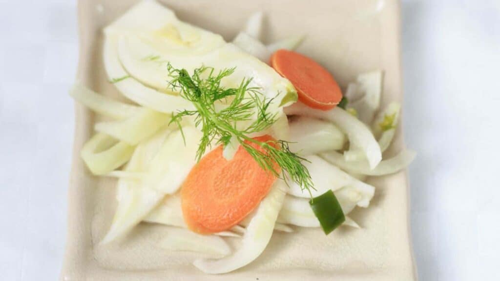 A plate with onions, carrots and dill on it.