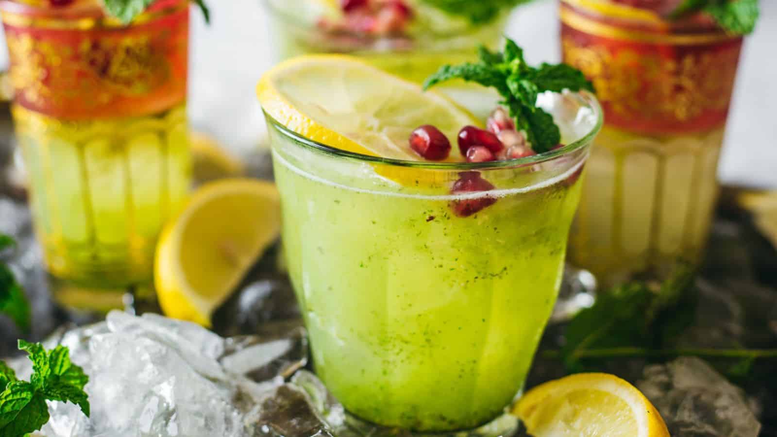 A glass of lemonade with pomegranate and mint leaves.