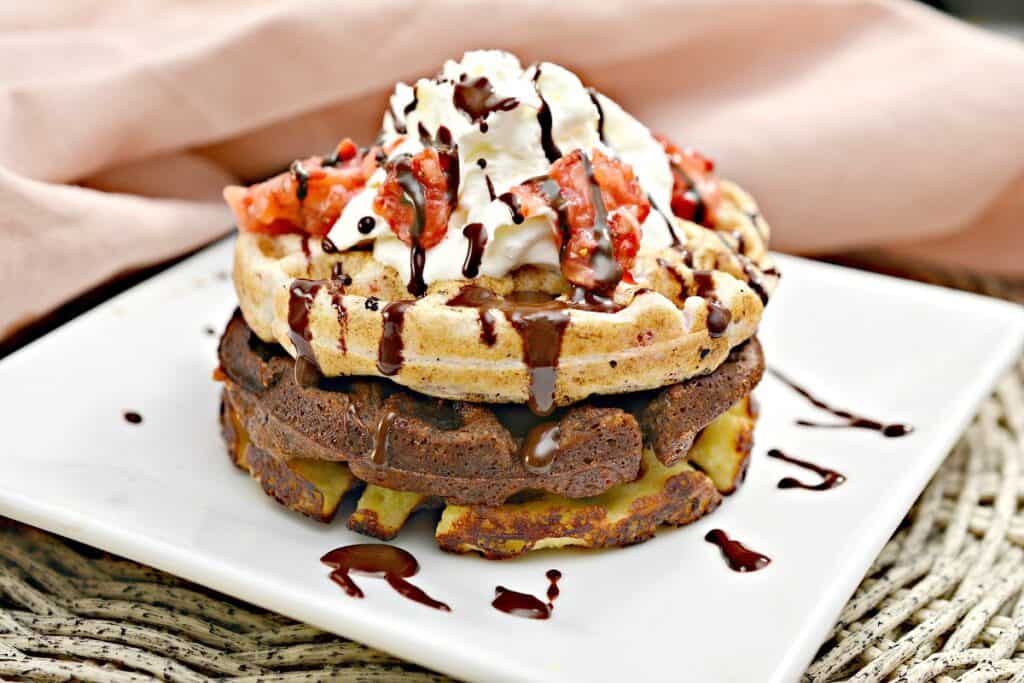 A stack of waffles topped with whipped cream and strawberries.