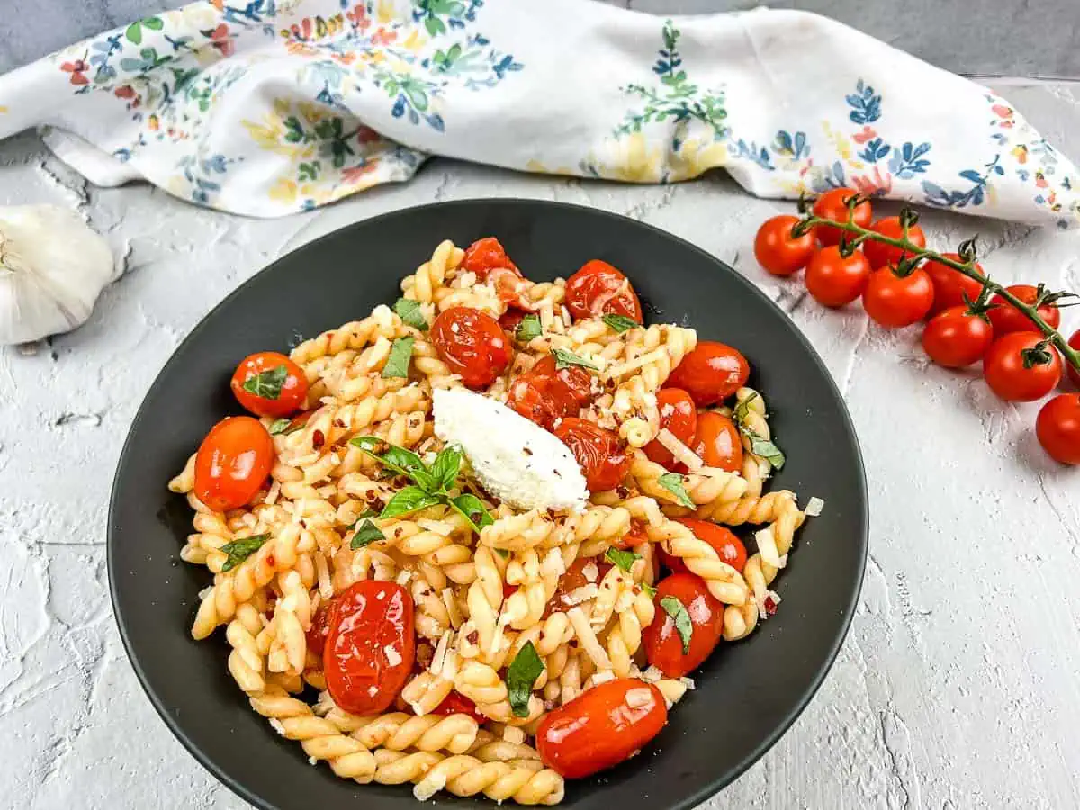 A bowl of pasta with cherry tomato sauce, cherry tomatoes, and garlic.