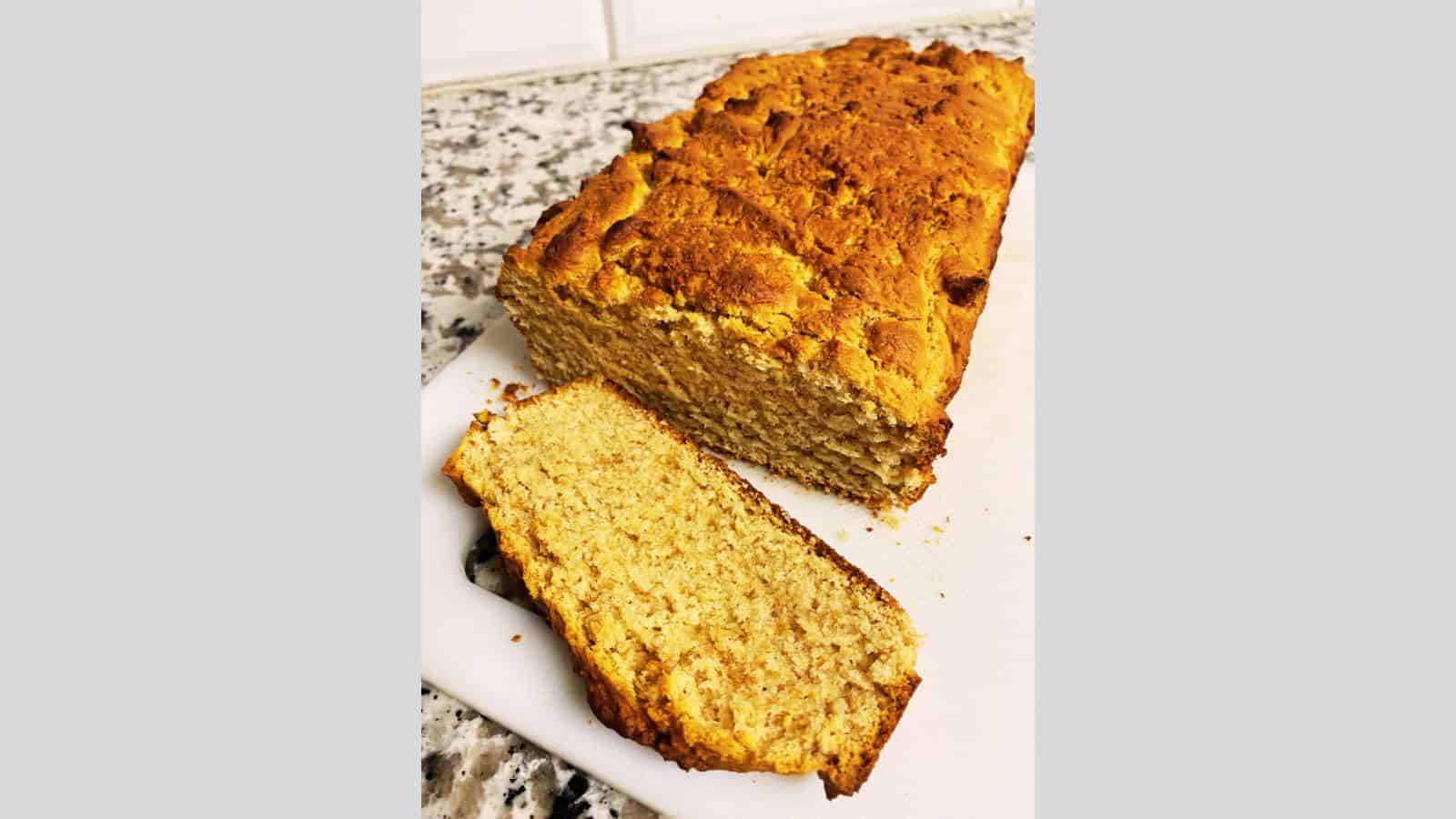 Loaf of peanut butter bread with one cut slice on white cutting board.