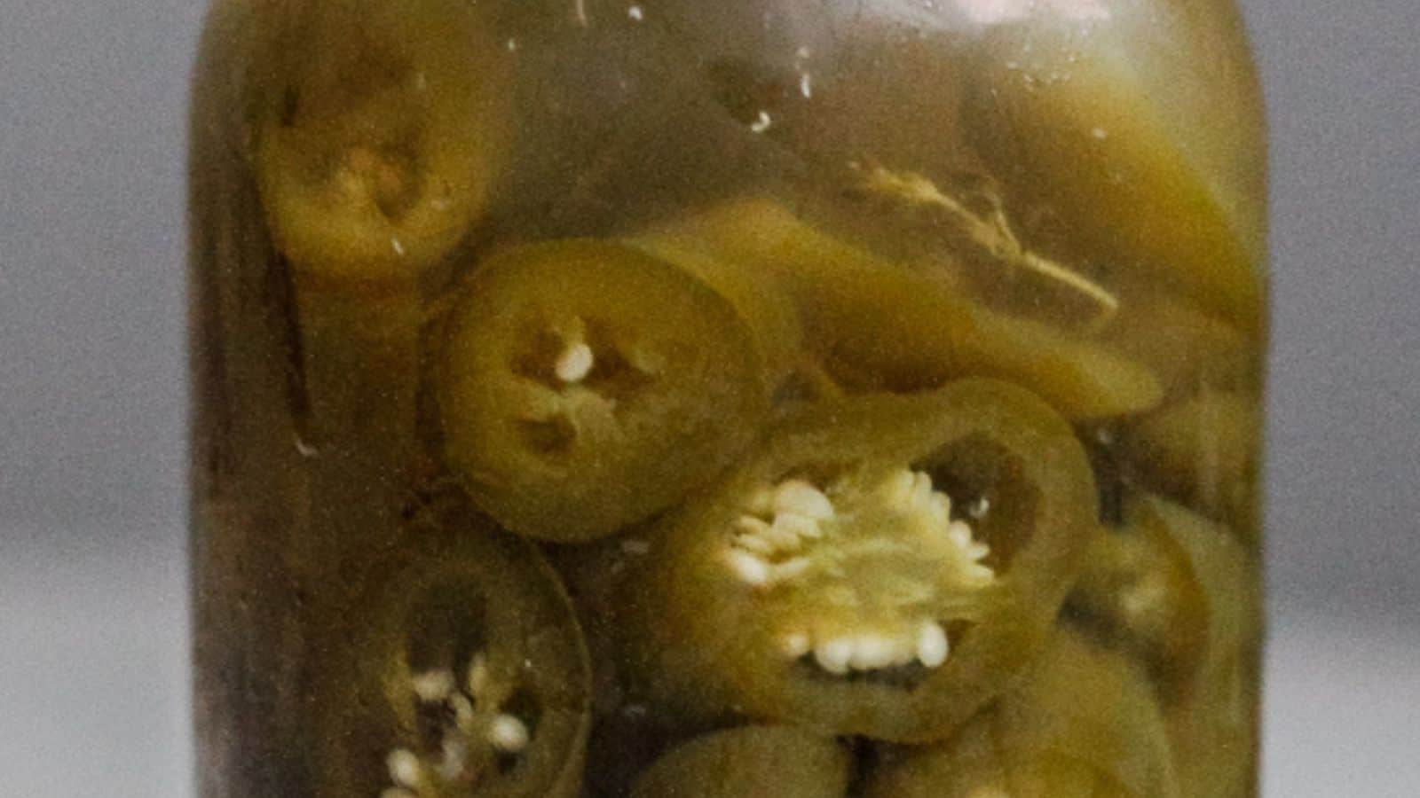 A jar of pickled jalapenos on a table.