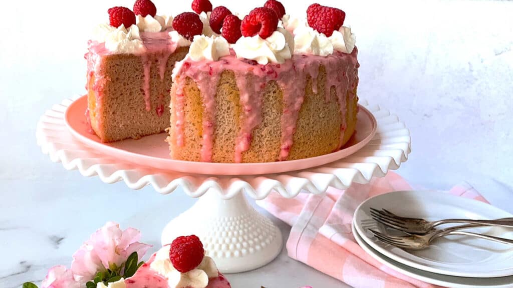 A pink cake with raspberries and icing on top.