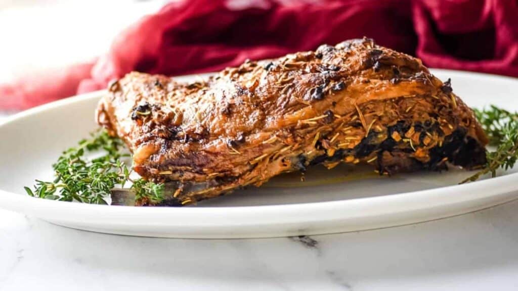 A piece of meat on a white plate with thyme.